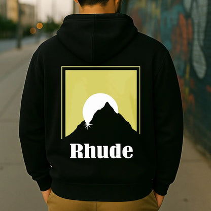 Person wearing a black hoodie with 'Rhude' logo against a graffiti-covered wall.